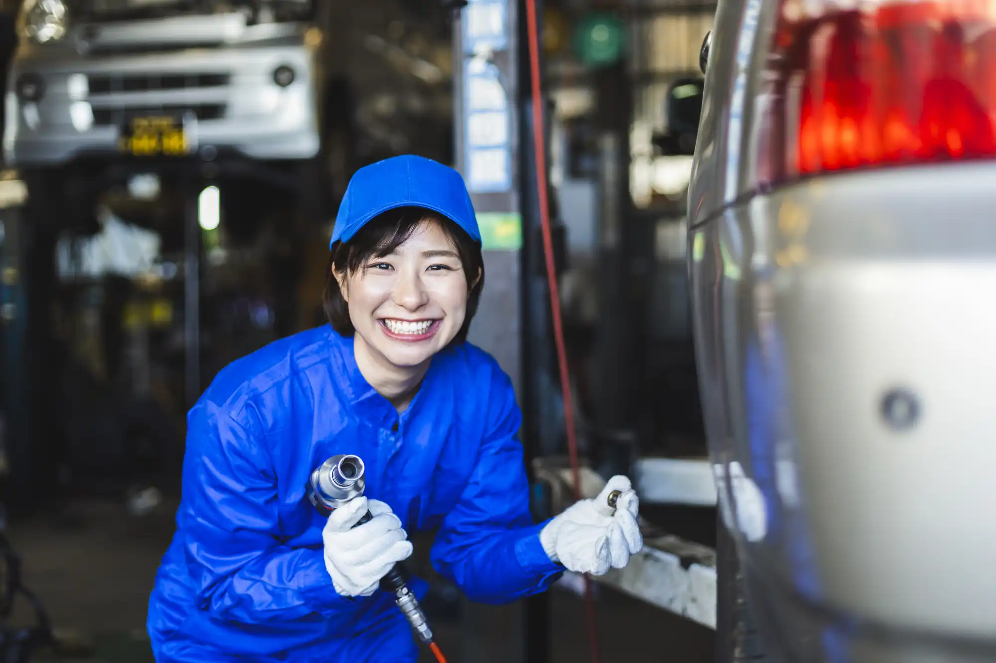 ホイールナットを外す青色の作業着を着た女性